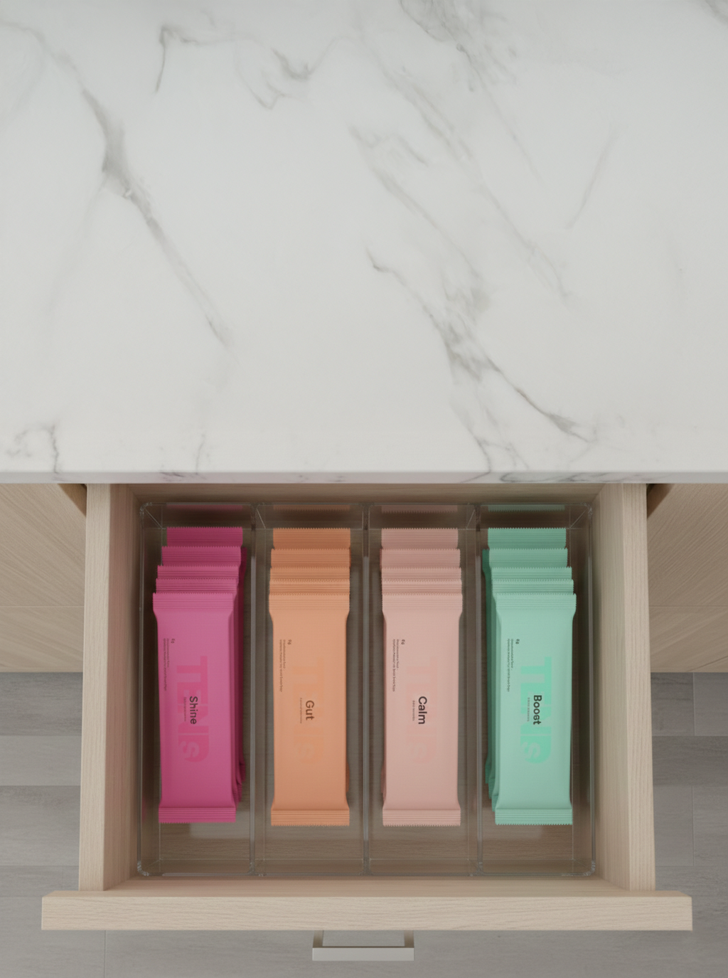 Top-down view of an open kitchen drawer with four compartments, each holding stacks of coloured hydration sachets labeled “Shine,” “Gut,” “Calm,” and “Boost.”