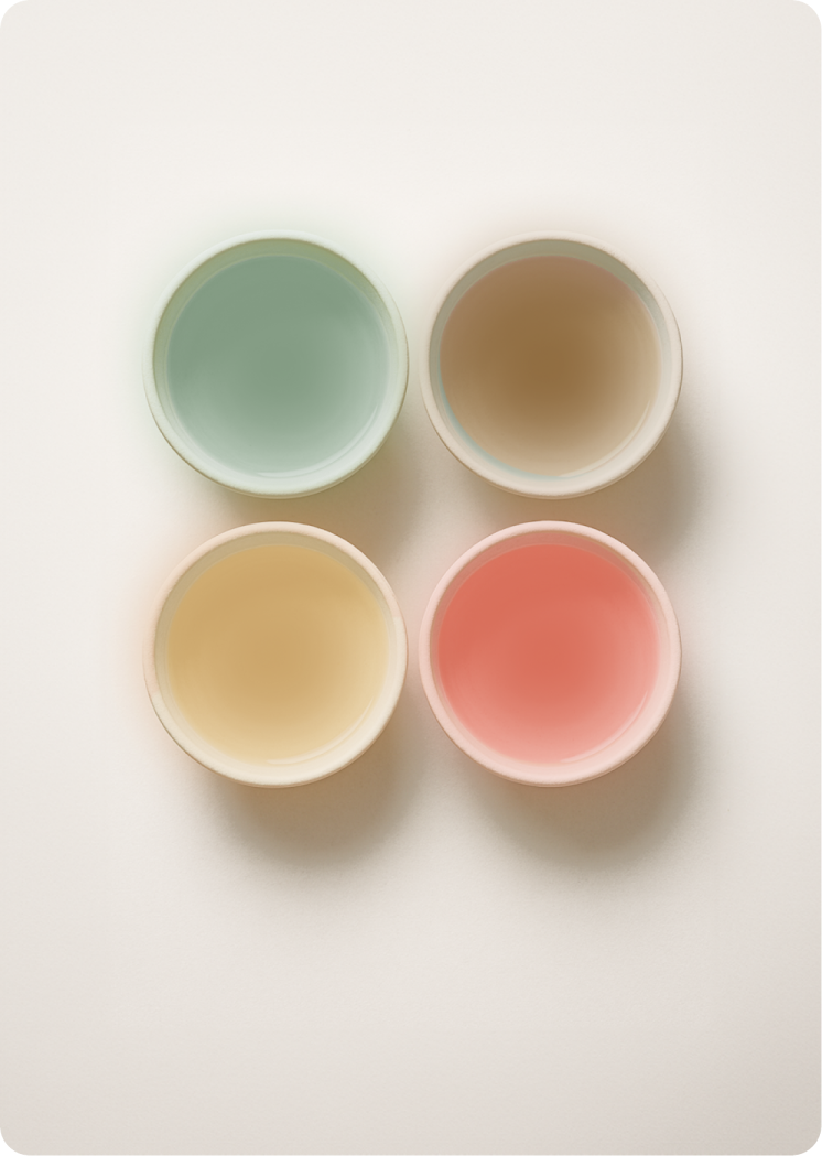 Top-down view of four small bowls arranged in a grid, filled with light green, beige, orange, and pink coloured water.