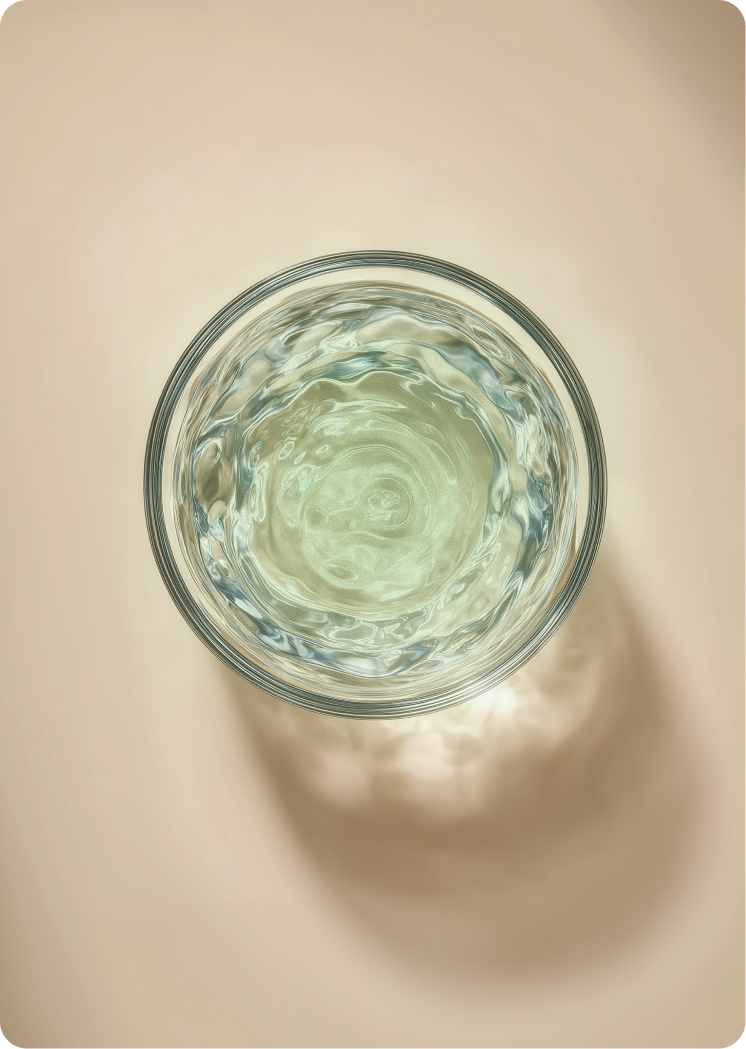 Top-down view of a clear glass filled with lightly tinted water, showing gentle swirling patterns.