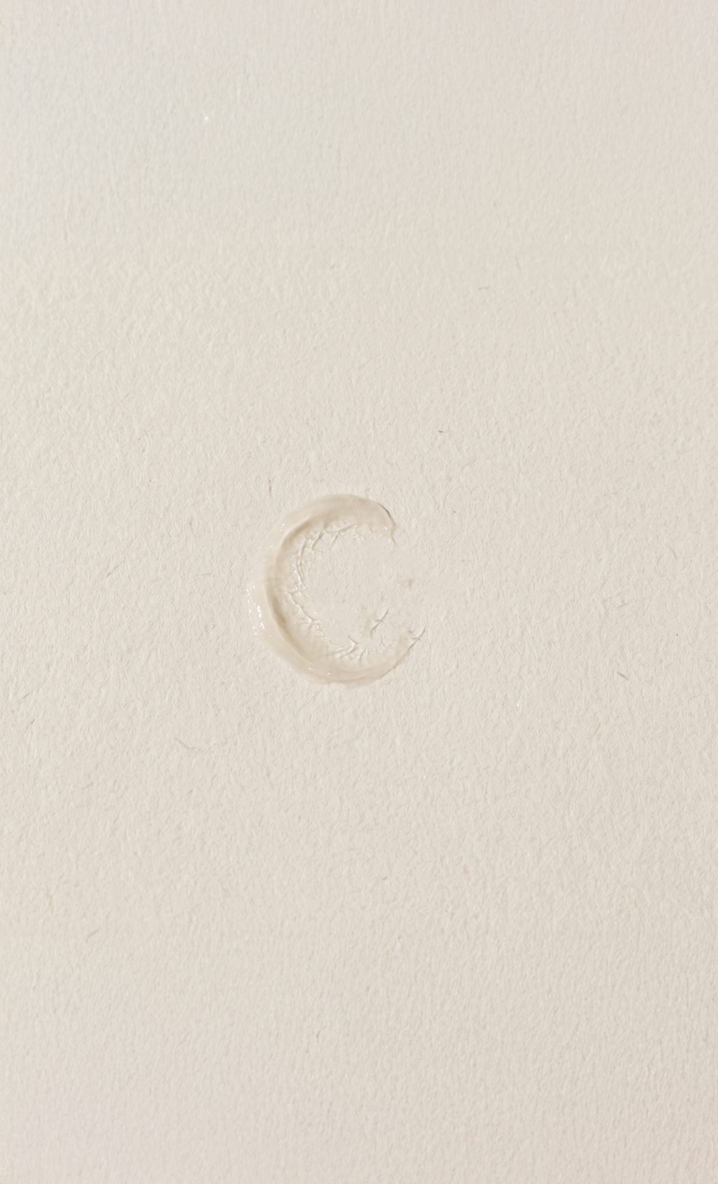A small, near-translucent ring of balm residue on a pale textured surface, almost invisible against the background .