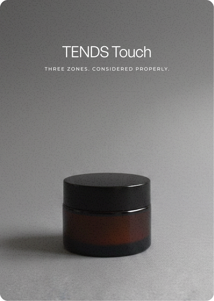 Amber glass jar with a black lid placed on a neutral textured surface, shown in soft, directional light against a minimal background.