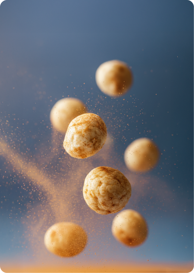 Air-popped lotus seed snacks suspended mid-air with fine seasoning particles floating around them against a soft blue background.